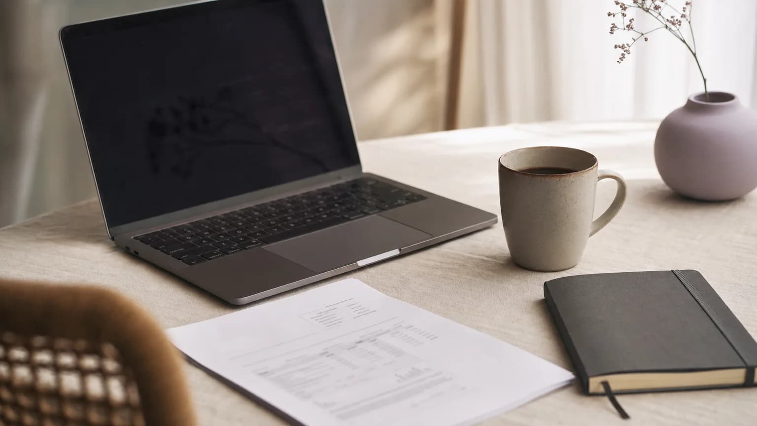 A freelancer's desk with a laptop and a printed invoice in warm morning light